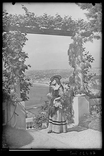 Femme en costume régional posant près d'une pergola. Vue sur le port