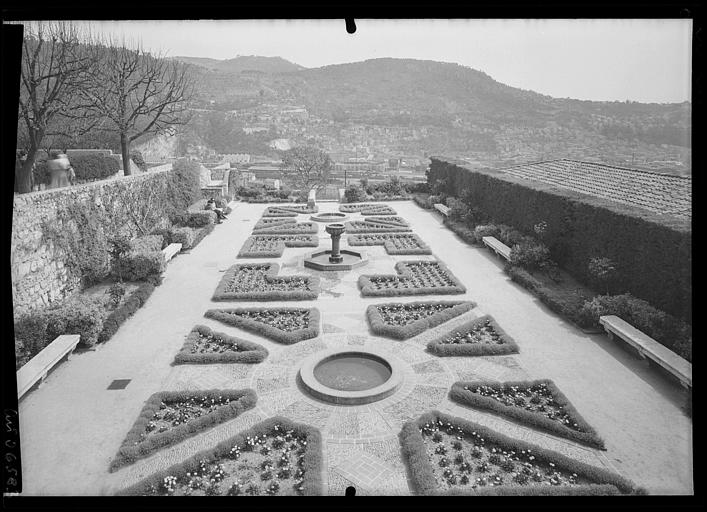 Les jardins : parterres fleuris, bassins au ras du sol, fontaine avec vasque sur pied