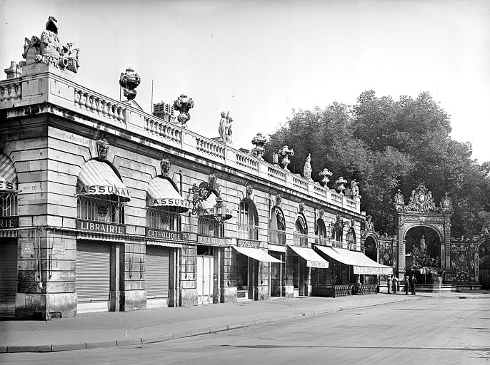 Vue de la place depuis l'angle nord-ouest : Pavillon de l'angle nord-est à un seul niveau. Commerces. Fontaine d'Aphrodite