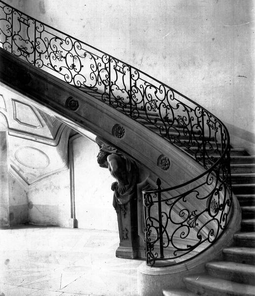 Rampe d'escalier en fer forgé et atlante en pierre soutenant l'escalier