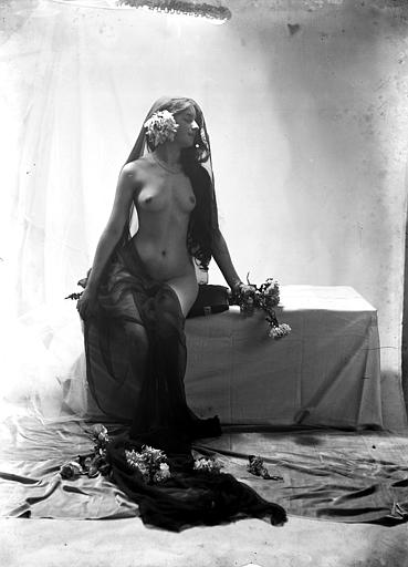Mise en scène d'un modèle féminin : jeune femme nue, vue de trois-quart face, assise sur un coffre et portant un voile noir