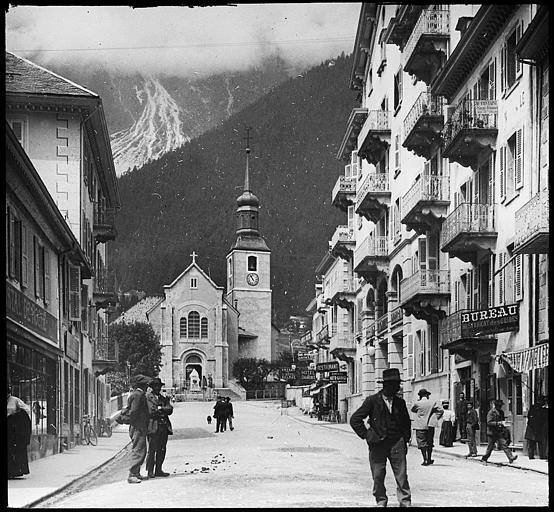 Le portail principal et le clocher ; nombreux personnages dans la rue