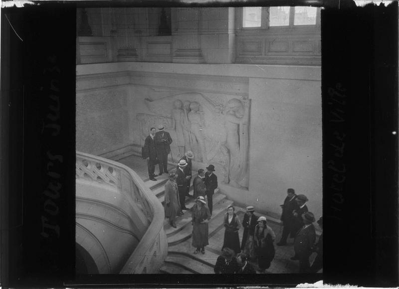 Intérieur : grand escalier depuis le premier étage et groupe de personnes