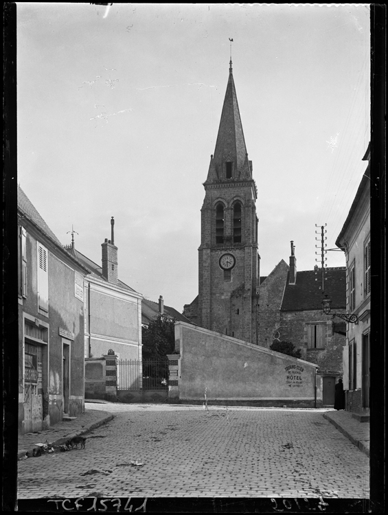 Clocher pris depuis la rue. Sur le mur de clôture, une enseigne indiquant un hôtel du Touring Club de France.