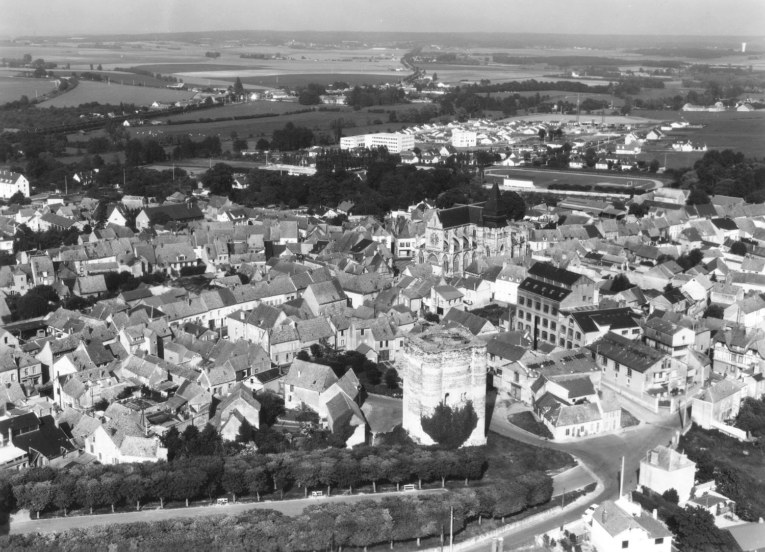 Vue aérienne d'Houdan. On localise parfaitement l'établissement Fouché, à droite de l'église et de la tour et la "maison normande", à l'extrème droite de l'image. Entre 1948 et 1972.