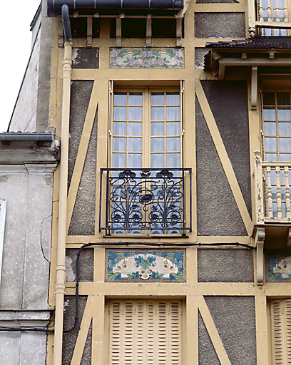 Détail de la fenêtre gauche du premier étage et du décor en céramique de la façade.