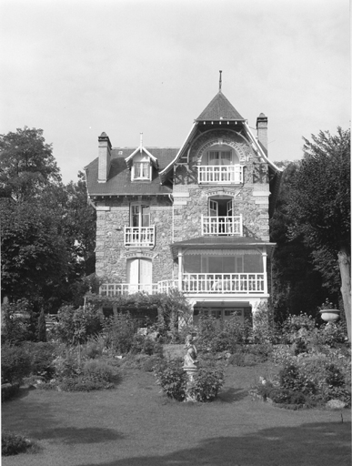 Vue de la façade sur jardin d'une maison de type anglo-normand construite en pierre meulière.