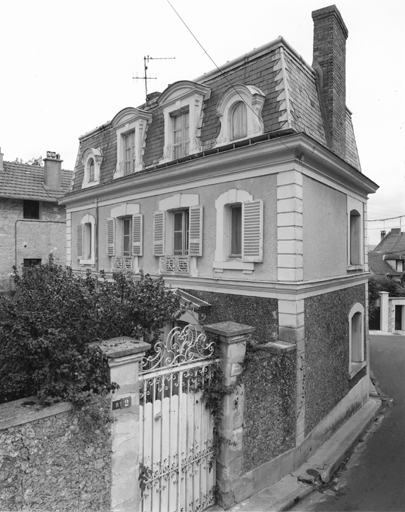 Vue de la maison, du mur de clôture et du portail en fer.