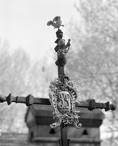 Cartouche et figurines en bronze chargeant la croix qui surmonte le tombeau.