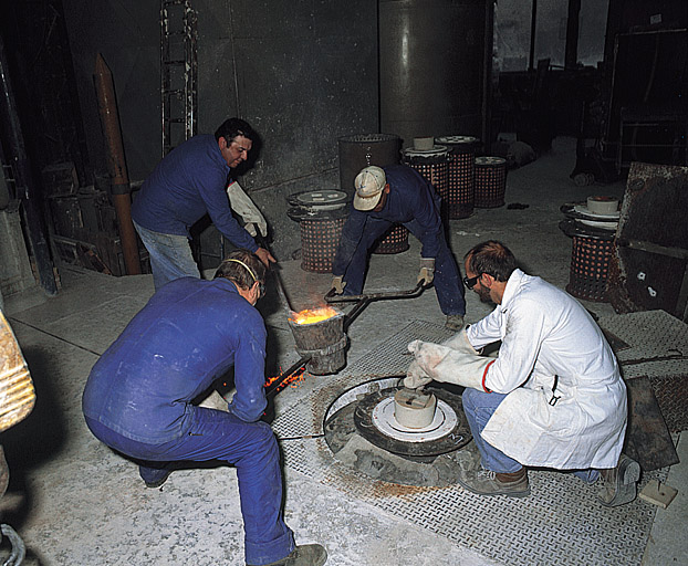 Coulée de bronze : déplacement du creuset vers le moule à cire perdue disposé dans une fosse et écrémage.