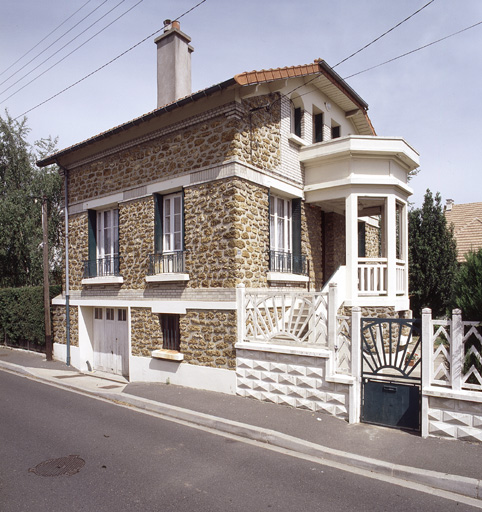 Vue d'ensemble ; le motif en ciment de la clôture est reproduit en métal à la porte d'entrée.