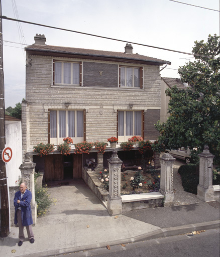 Vue d'ensemble. La façade porte un décor de revêtements et de sculptures, ainsi que les piliers de la clôture.