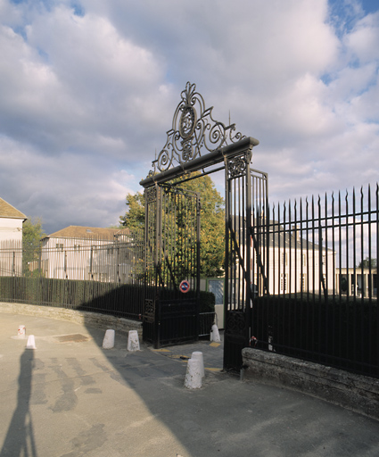 Vue du portail et de la grille en demi-lune fermant la cour d'honneur ; dans le médaillon, initiales de la famille Chodron de Courcel (CC).