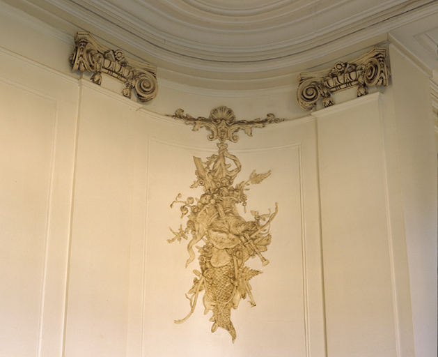 Vestibule : détail d'un panneau décoratif en stuc (chute d'armes) entre deux chapiteaux ioniques.
