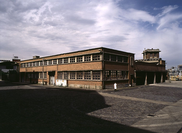 Ensemble de bâtiments situés sur le flanc nord-est de la cour, comprenant les ateliers de mécanique et de menuiserie, les garages et la 'boulangerie' (fournil et moulin d'essais) surmontée d'une tourelle.