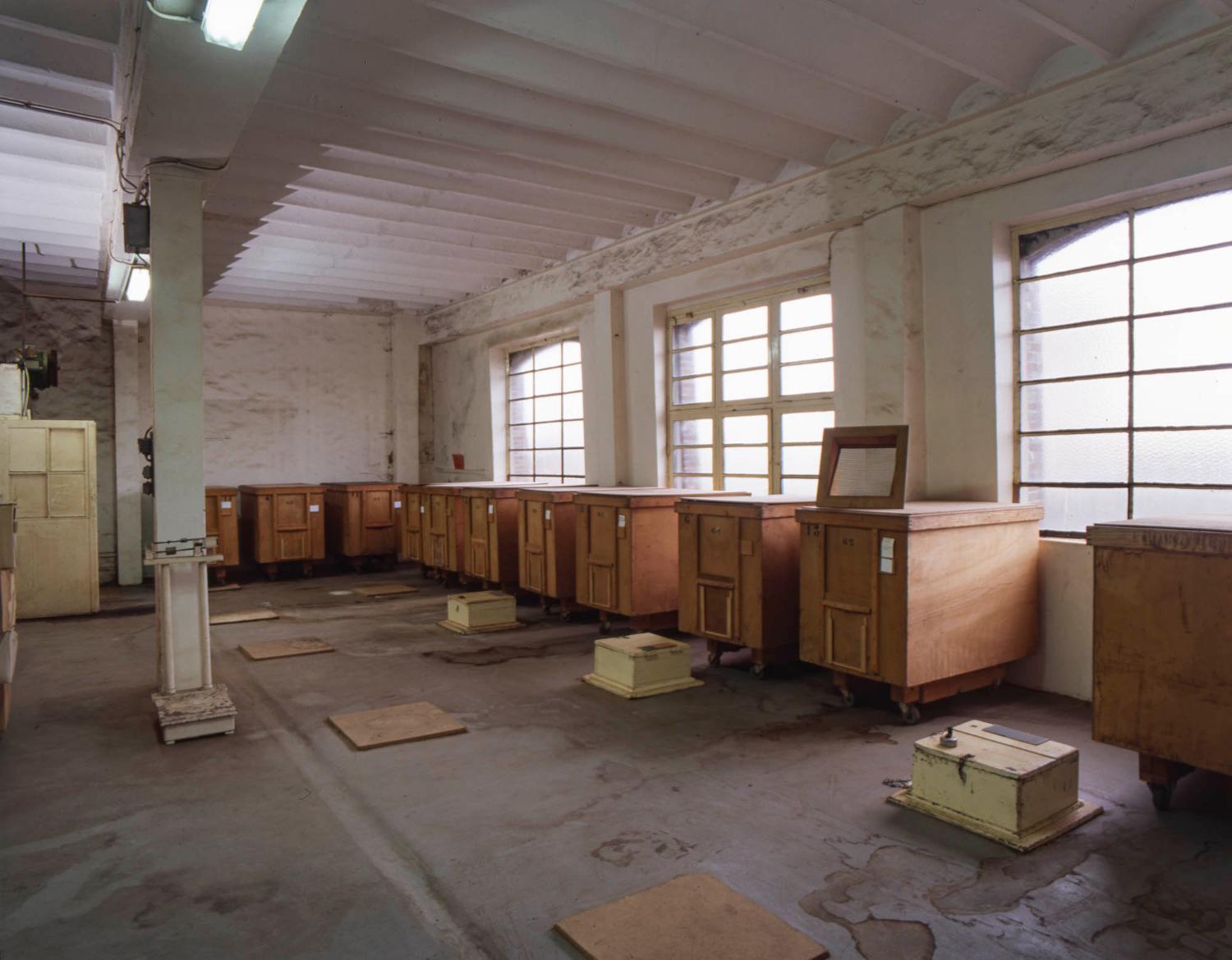 2e étage du bâtiment principal. Alignement de wagonnets en bois servant au transport des plantes, posé sur l'un d'eux un filtre. Les trappes au sol permettaient d'alimenter des machines à conditionner, installées à l'étage du dessous.