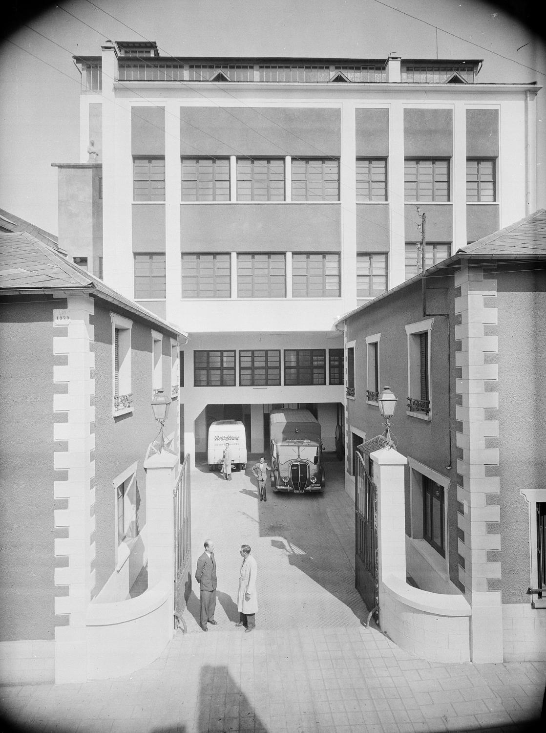 Vue de l'entrée des établissements Fouché, au fond le bâtiment principal, devant lequel est garée l'ambulance du tour de France. En haut du chainage d'angle de gauche, incription "EFF [établissement Fouché Frères], 1929".