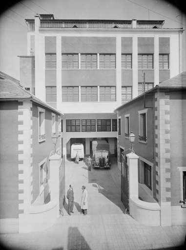 Vue de l'entrée des établissements Fouché, au fond le bâtiment principal, devant lequel est garée l'ambulance du tour de France. En haut du chainage d'angle de gauche, incription 'EFF [établissement Fouché Frères], 1929'.