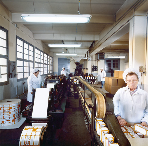La chaine de conditionnement du 2e étage du bâtiment principal en activité. A gauche, la machine fabriquant des boites pour le vrac (à partir de papier cartonné imprimé et de papier fin formant le sac intérieur). Les boites étaient ensuite remplies de tisane à l'aide de la machine au fond (sous le grand entonnoir) et revenaient sur un tapis roulant (le temps que la colle sèche) pour être stockées dans des cartons d'expédition.