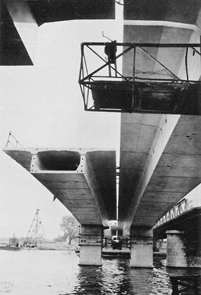 Vue du pont de béton précontraint en cours d'assemblage, parallèlement au vieux pont métallique de la fin du XIXème siècle visible sur la droite et provisoirement conservé malgré les dommages provoqués à l'une des piles par un bombardement de 1944.