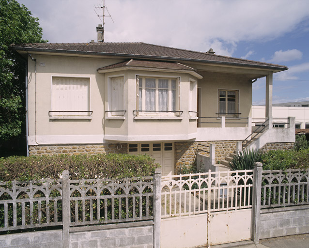 Vue d'ensemble de la maison ; elle porte la signature de l'entrepreneur R. Bouscal (Orly). Une haie vive double la clôture en ciment armé du type 'Arceaux'.