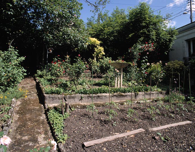 Vue partielle du jardin, à gauche de la maison ; au fond à gauche, un kiosque recouvert de végétation très peu visible sur la photo.