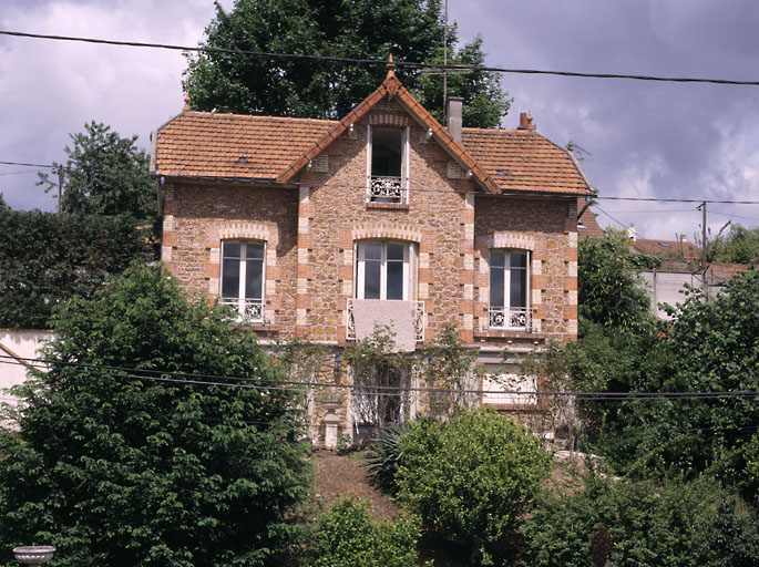 Vue d'ensemble de la maison ; un jeu de briques blanche et rouge souligne les angles et le contour de baies.