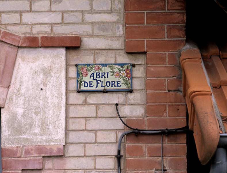 Plaque émaillée portant l'appellation 'Abri de Flore' sur la façade vue depuis la rue