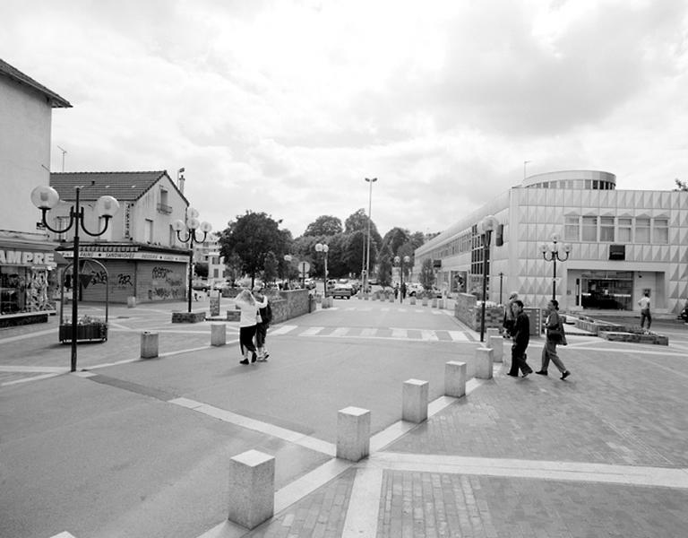 Vue perspective de la place de l'Orge et de la place Anatole France. L'intersection de la Grande Rue avec l'ancien cours de l'Orge aujourd'hui couverte est devenue la place de l'Orge. A l'arrière plan, le parking occupe l'ancienne place du marché et le bâtiment de la Société Générale occupe l'emplacement de l'ancien moulin.