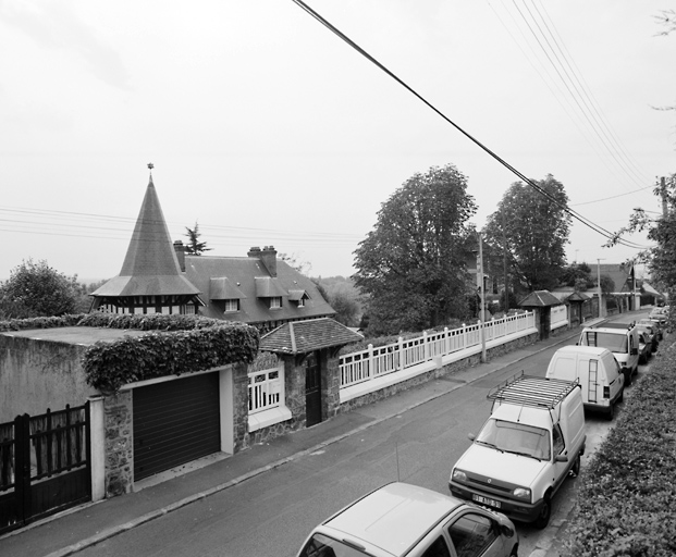 La maison derrière sa clôture percée de deux portes à chaperon couvert de tuiles.