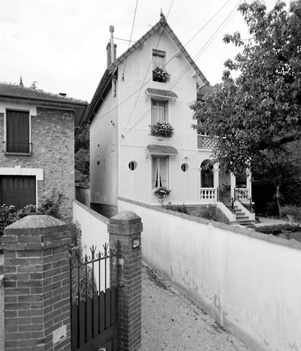 Vue d'ensemble de la maison. Un décor de faux pans-de-bois anime la façade. Deux autres maisons, à proximité, possèdent la même loggia à trois arches surmontée d'une terrasse.