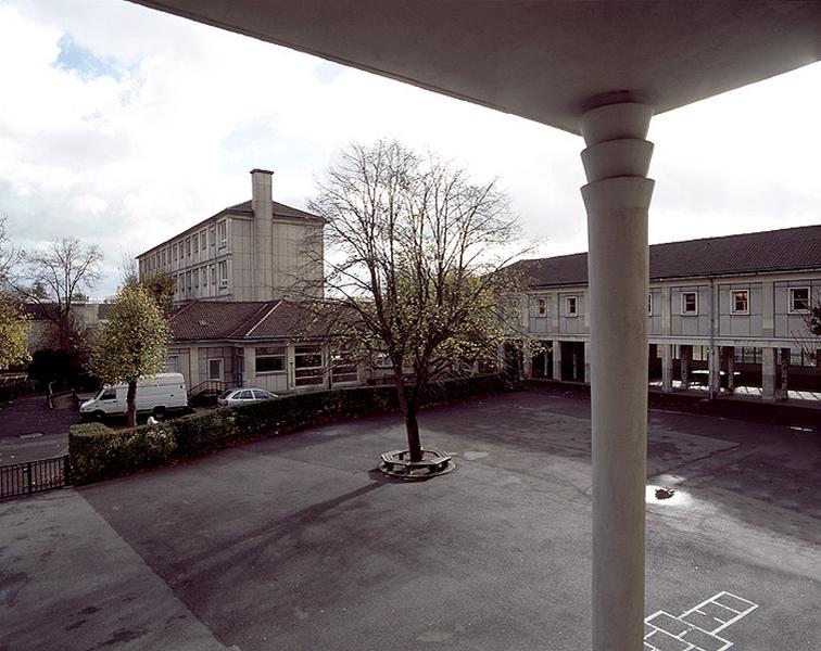 Vue de la cour de récréation, du préau et de la cantine du groupe scolaire pris du perron du pavillon des éditions du Cerf.