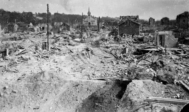 Ruines et trous de bombes dans le quartier du Val ; à l'arrière plan, la façade de l'église paroissiale encore debout ; 1944.