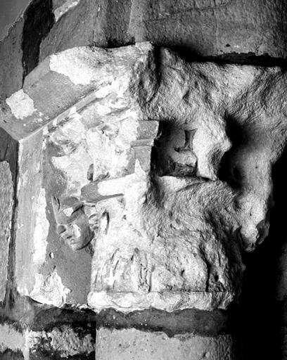 Chapiteau sculpté de la 5eme paire de colonnes jumelées, côté ouest (vers la salle capitulaire). Le chapiteau est complètement érodé, seul reste visible une tête de profil, sculptée en léger relief.