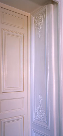 Vue d'ensemble d'un lambris de hauteur ornant l'ébrasement d'une porte entre le salon de compagnie et la chambre à alcôve.