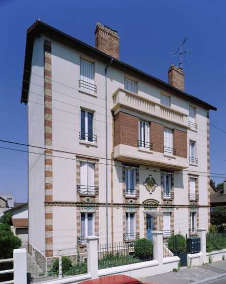 Vue d'ensemble de l'immeuble vraisemblablement surhaussé de deux niveaux dans les années 50. Le rez-de-chaussée et le 1er étage portent un décor de céramique à dominante jaune-orangé.