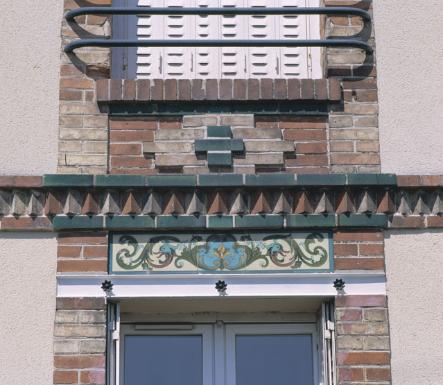 Détail du décor (frise de céramique et bandeau de briques disposées en dents d'engrenage) situé au-dessus des fenêtres.