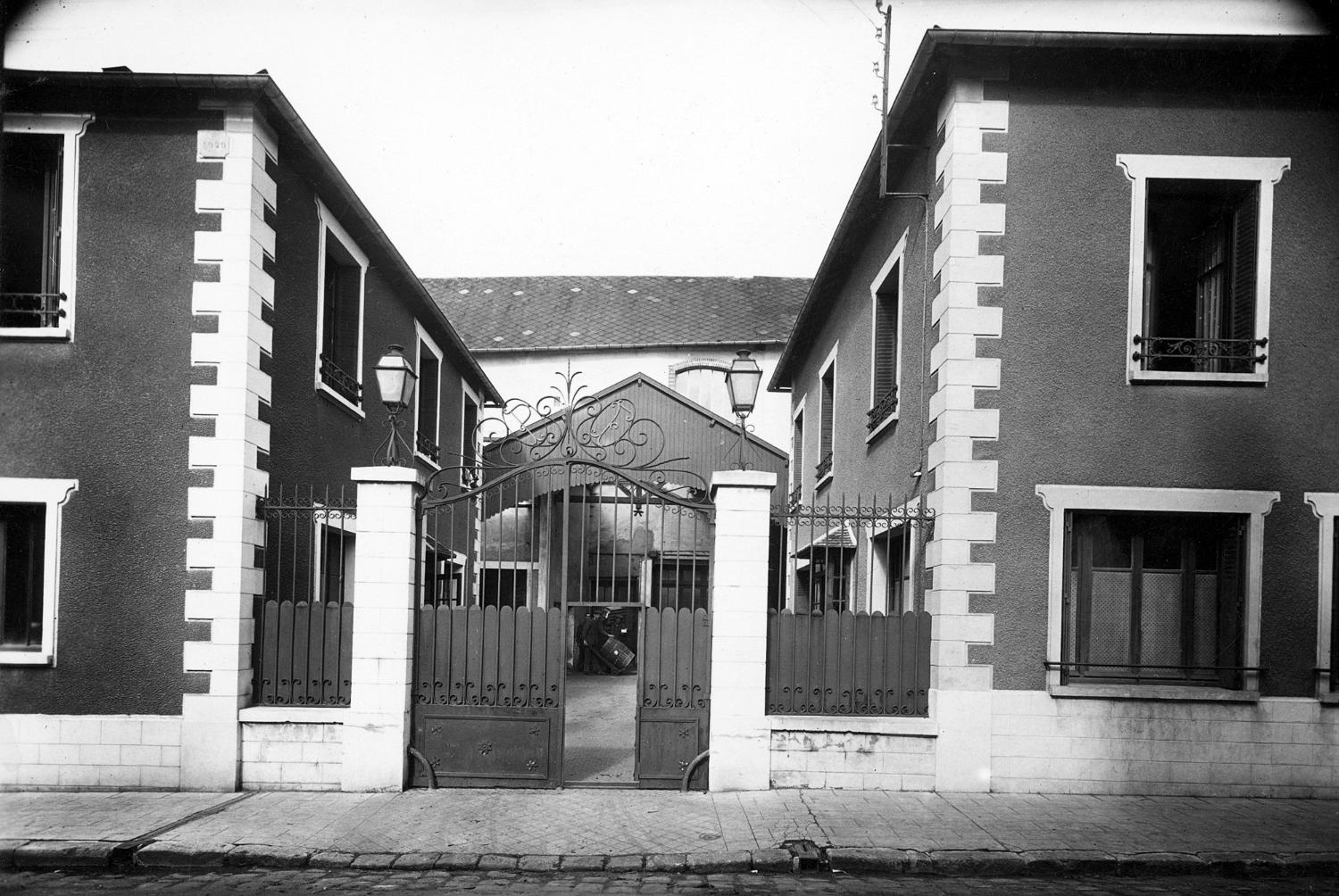 Vue de l'entrée de l'usine après 1929, date de la surélévation des deux maisons latérales et avant la construction du bâtiment principal, au fond, à la fin des années30.