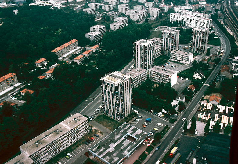 Vue aérienne : partie basse du parc du lycée Saint-Charles, immeubles et pavillons à toitures de tuile de la Cité du Parc-d'Athis et immeubles situés autour des cours Joseph-Dewalle et de la place du Languedoc, entre la zone verte de l'Orge et la rue Edouard-Vaillant.