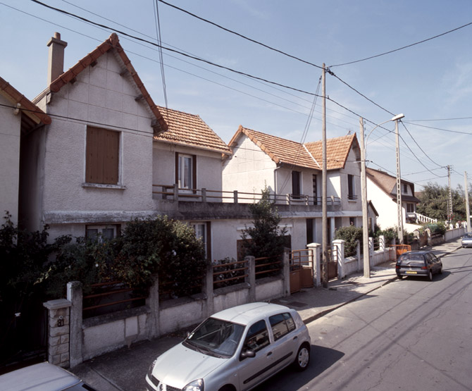Maisons (construites sur le même plan) reliées par leurs garages dont le toit forme terrasse.