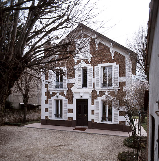 Vue d'ensemble : une modénature de plâtre et d'enduit anime la façade principale de cette maison de villégiature du coteau ; corniches, bandeaux, encadrements et chaînes d'angle peints en blanc se détachent sur le mur rocaillé.