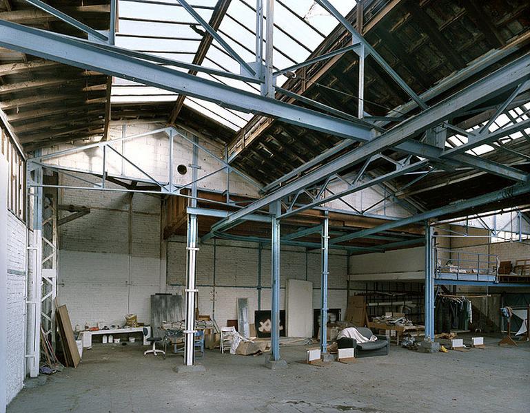 Intérieur de l'usine, depuis l'emplacement de l'atelier d'ébarbage. au fond à gauche, l'emplacement des fours ; au centre, l'aire de coulée surmontée du rail de soutien et de guidage des poches de métal en fusion ; au fond à droite, l'emplacement de l'établi des mouleurs et la grande étuve pour les moules.