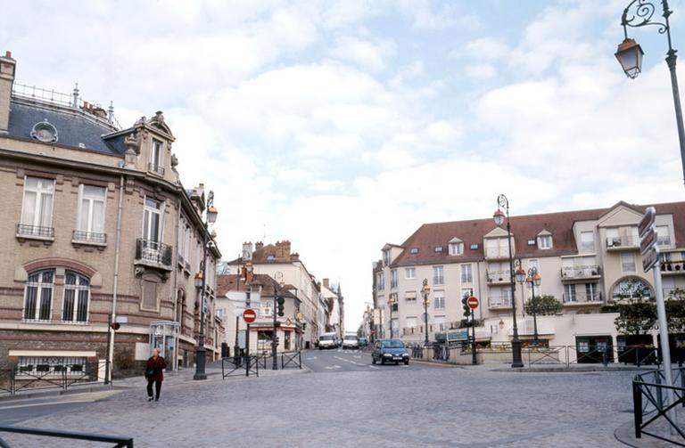 La place Porte-de-Paris, vue depuis la rue Carnot. Cette place occupe l'emplacement des anciennes fortifications d'agglomération (détruites au 18e siècle), qui marquaient la limite entre la ville close et la paroisse Saint-Barthélemy. Au centre, la rue Saint-Barthélemy est l'ancienne route de Paris, qui monte à flanc de coteau vers la préfecture et l'hôtel du département (ancienne abbaye Saint-Père). A droite, une opération immobilière du dernier quart du XXe siècle a remplacé l'ancienne école Saint-Barthélemy, du 19e siècle.