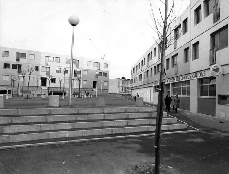 Vue prise en 1976. La place du Trident et son échelonnement de marches conduisant à un rond-point d'arbres rythmé de bancs publics, au second plan on aperçoit un bâtiment du groupe scolaire Dorgelès.