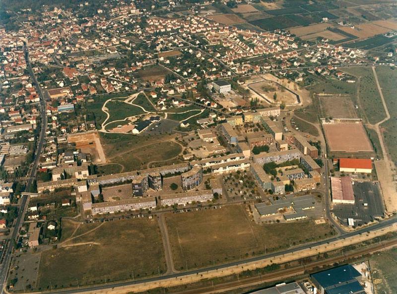 Vue aérienne de la partie est du quartier. A l'arrière plan, le village de Chanteloup. Le foyer de travailleurs célibataires est détruit. Seuls les deux bâtiments reliant la place du Béguinage à celle des Arcades ont été rénovés.