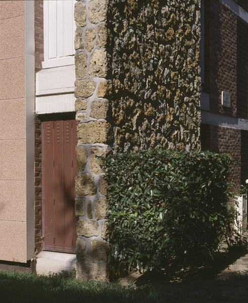 Extrémité de façade montée en maçonnerie de meulière ; au-delà, la façade est en brique apparente sur une ossature en béton armé.