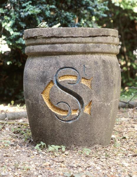 Jardinière en ciment dans le parc de l'hôpital portant les initiales de saint Camille entrelacées.