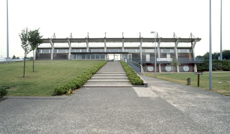 Vue d'ensemble du bâtiment des tribunes depuis le bas de la rampe d'accès.