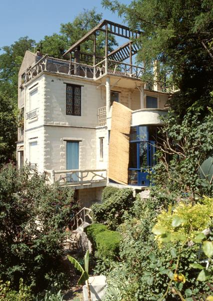 Vue de la maison depuis le jardin en contrebas des différentes terrasses étagées ornées de décor faux-bois en ciment.
