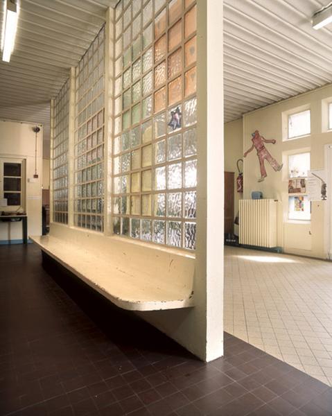 Vue intérieure du hall, banc en béton moulé le long d'une cloison en pavés de verre.